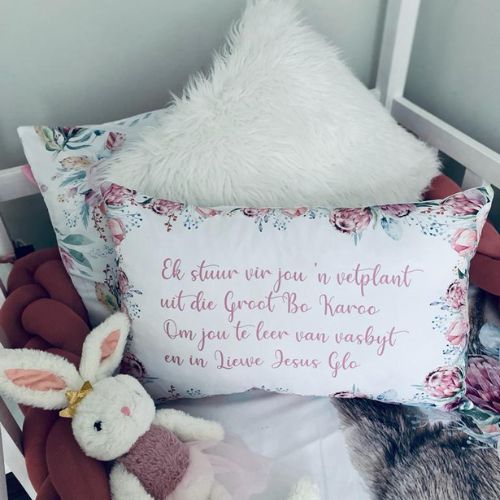 Floral pillow with text on a chair with a plush toy