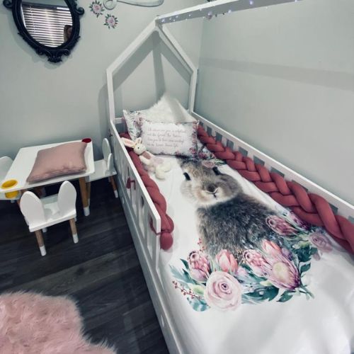 Children's room with a bed featuring a floral and animal design, pink accents, and small table with chair.