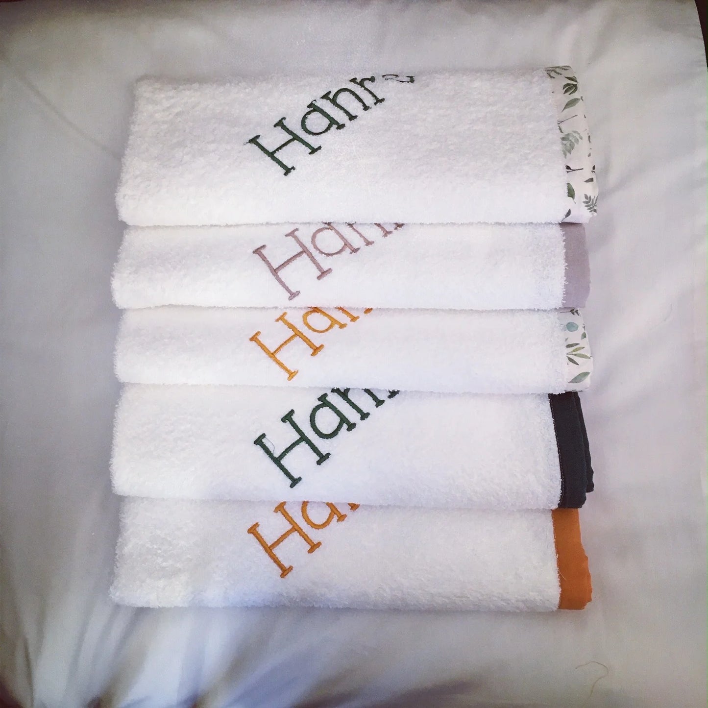 Stack of white Burp Cloths towels with embroidered names on a white background