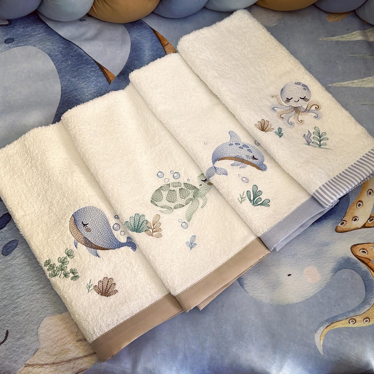 Set of embroidered towels with sea creature designs on a textured surface.