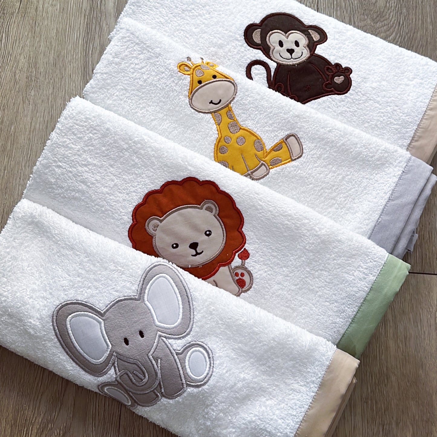 A set of white burp cloths with embroidered animals including a monkey, giraffe, elephant, and lion.