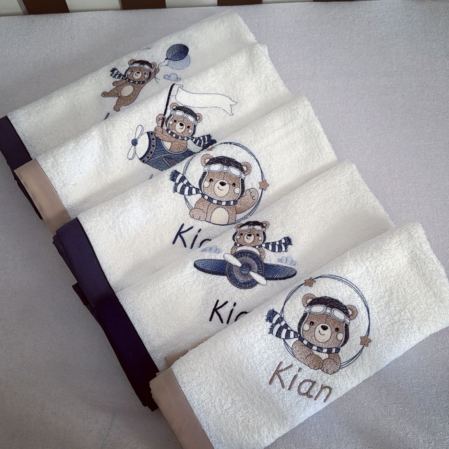 Set of towels with embroidered teddy bear designs and the name 'Kian' on a light gray background.