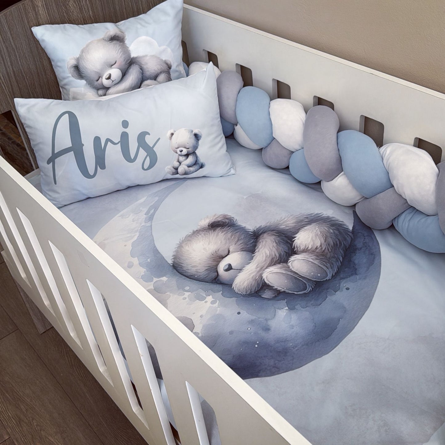 Baby crib with teddy bear-themed bedding and personalized pillow.