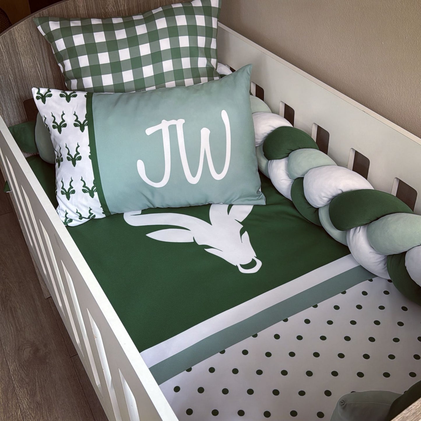 Baby crib with green and white bedding, monogrammed pillow, and checkered pillow.