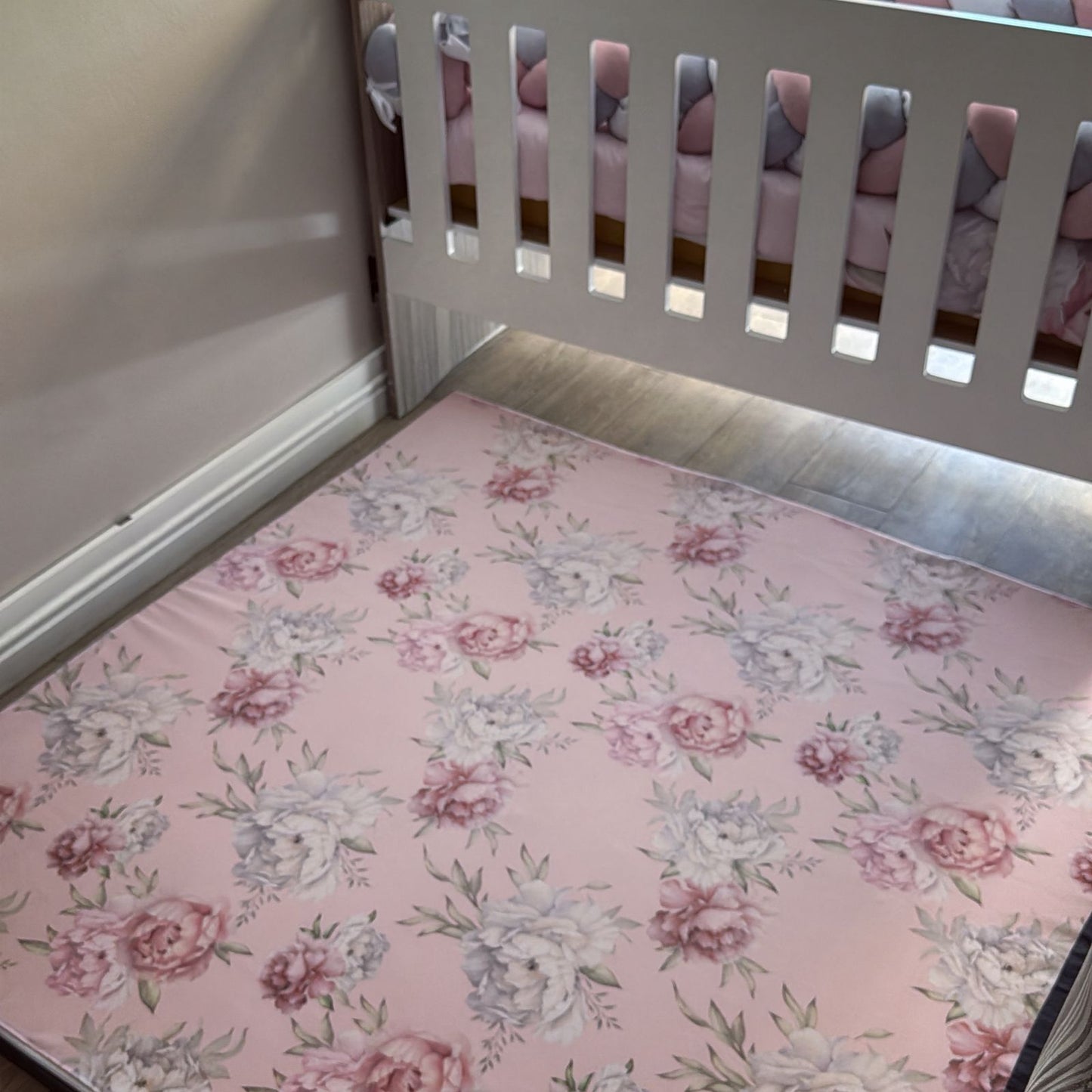 Floral mattress cover on a crib with a pink and gray patterned blanket.
