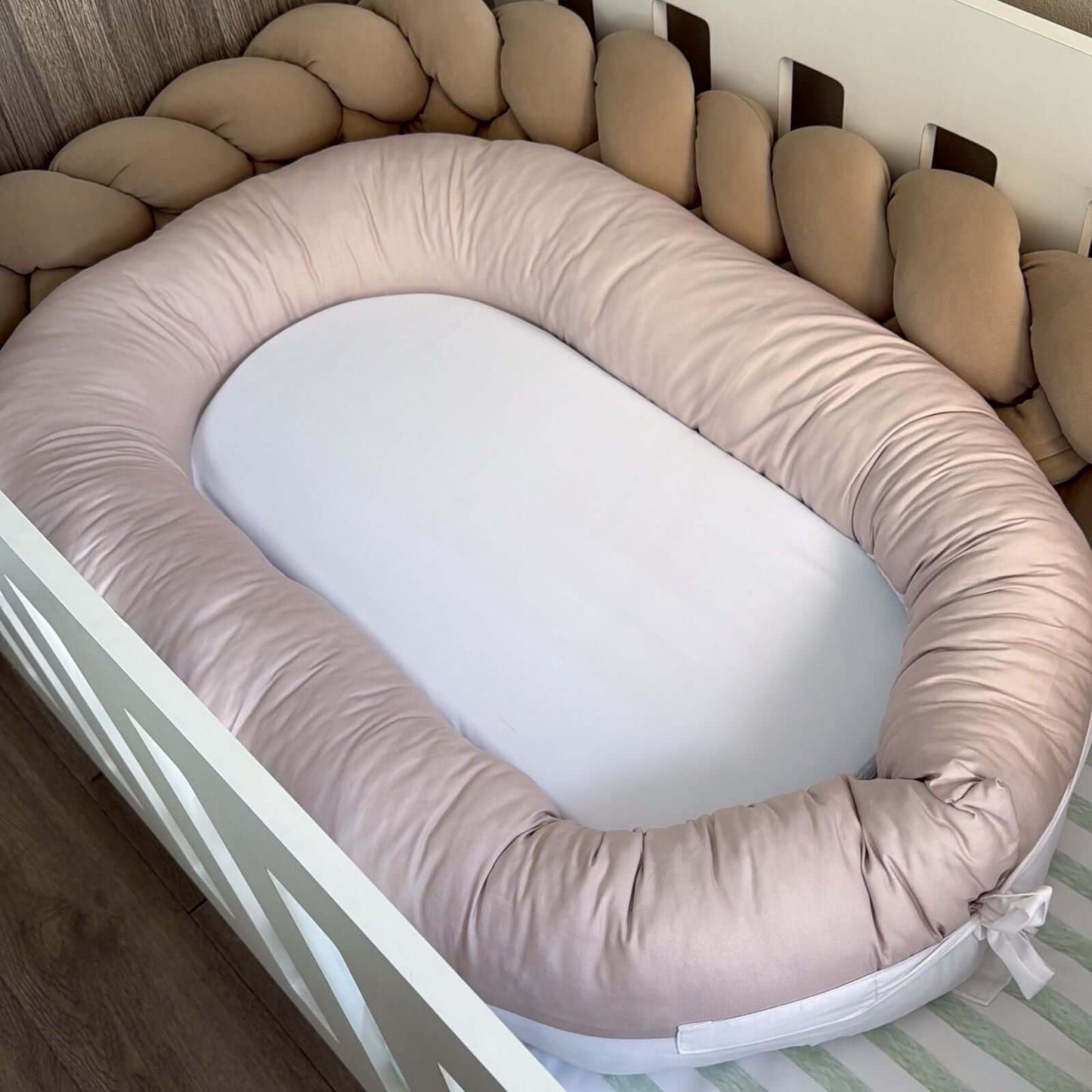 Baby nest with beige cushioned sides inside a crib