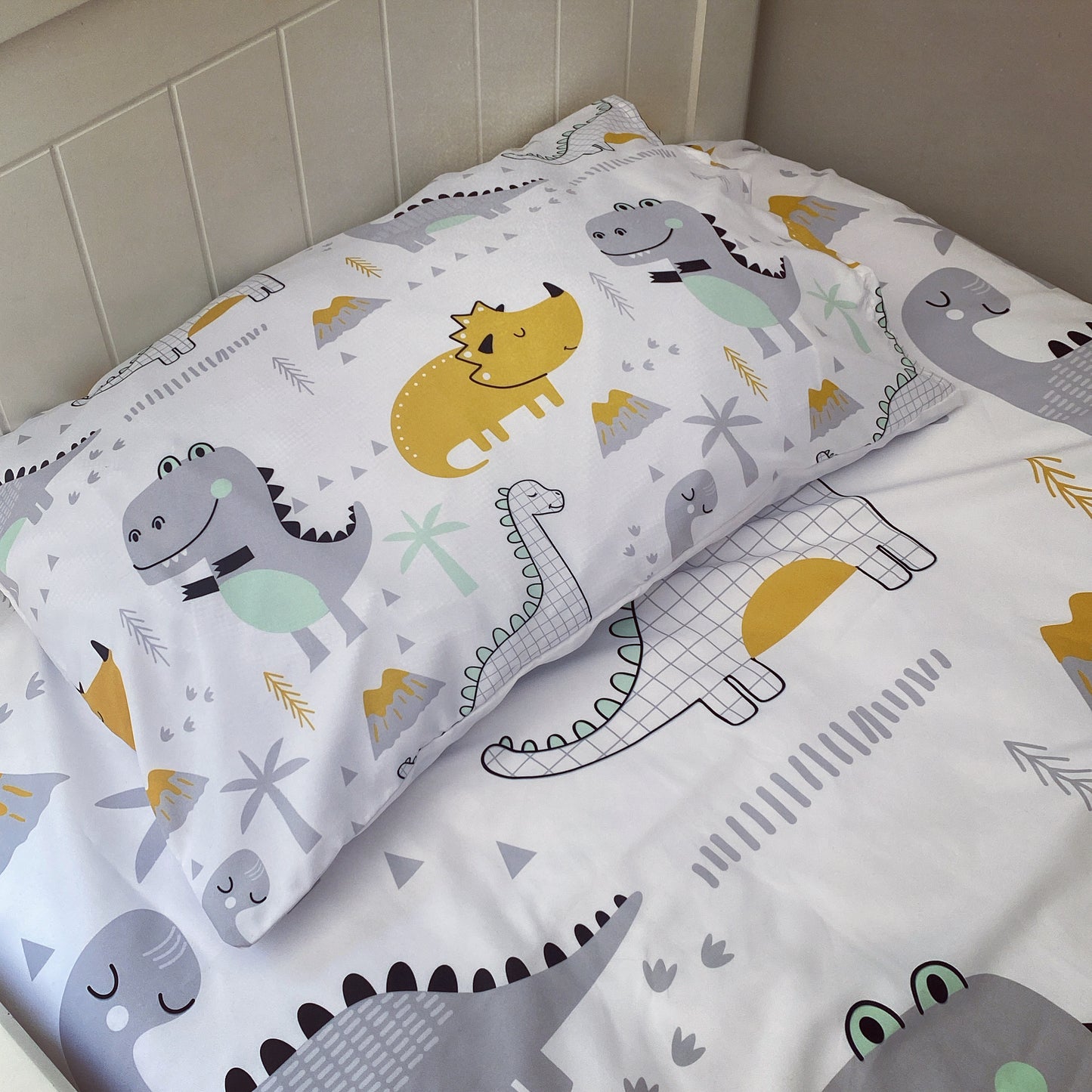 Children's dinosaur-themed pillowcase and sheet set on a bed.