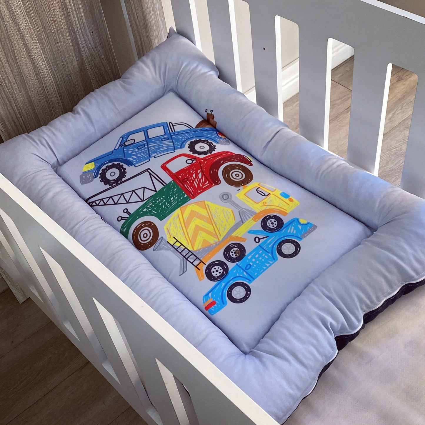 Crib bumper with colorful truck design on a white crib