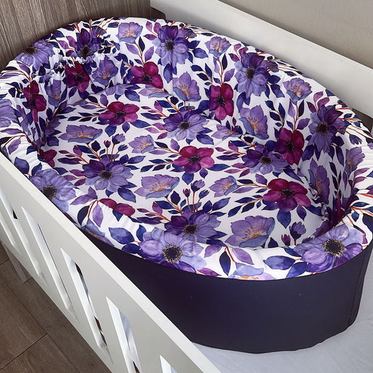 Floral-patterned baby bassinet cover with purple and pink flowers on a white crib.