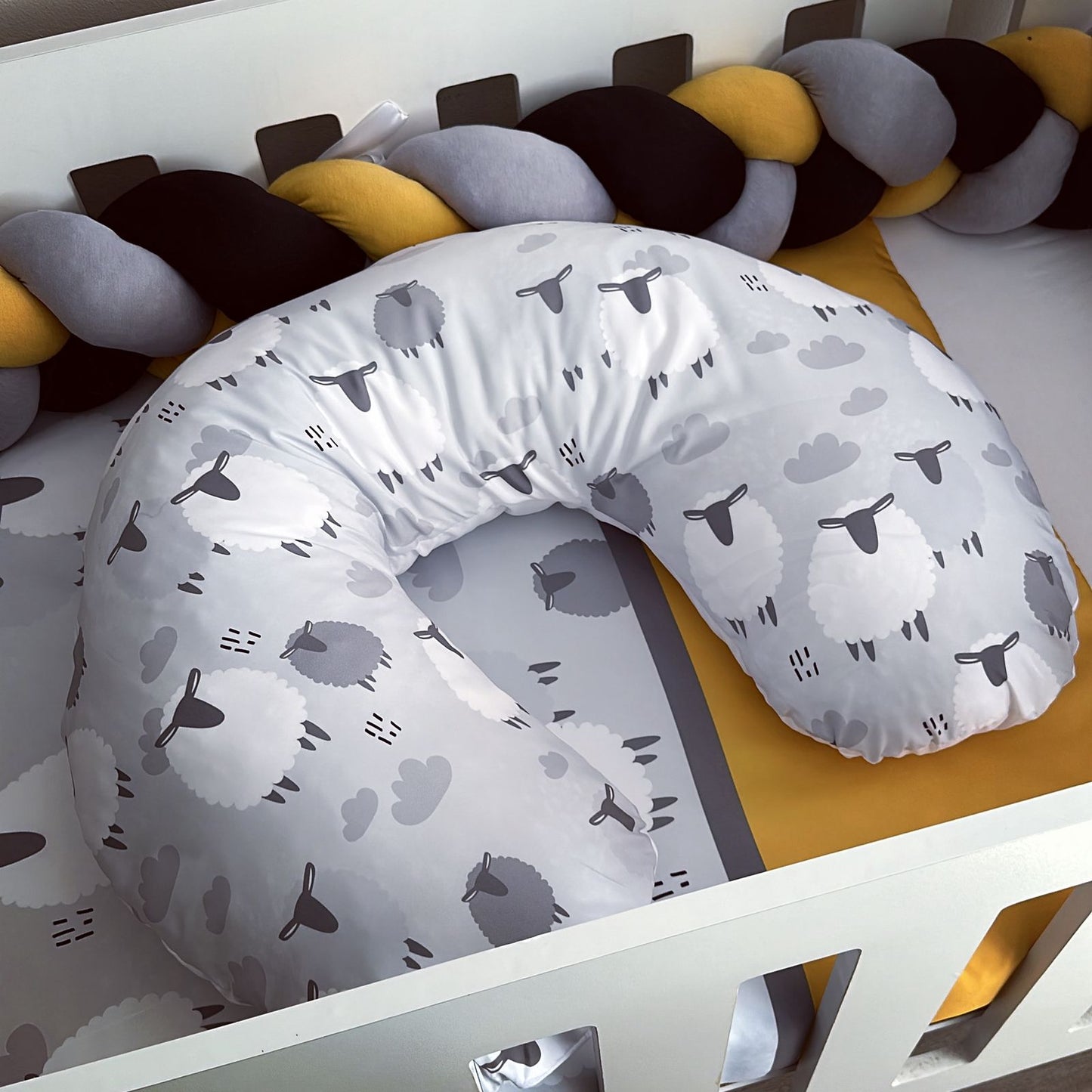 Gray U-shaped pillow with animal pattern on a white crib