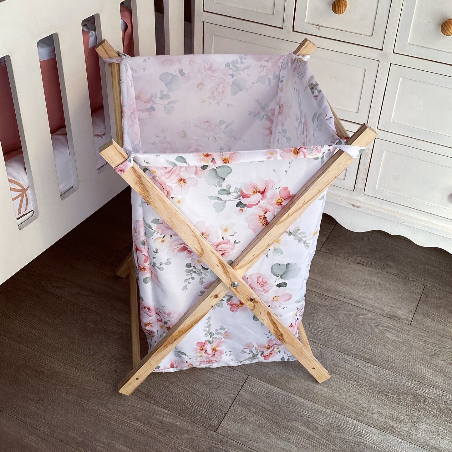 A wooden laundry basket with a pink floral pattern, featuring side handles and a five-point star base.