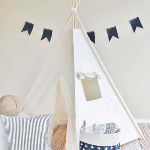 Children's teepee with pillows, a basket, and decorative flags on a plain wall.