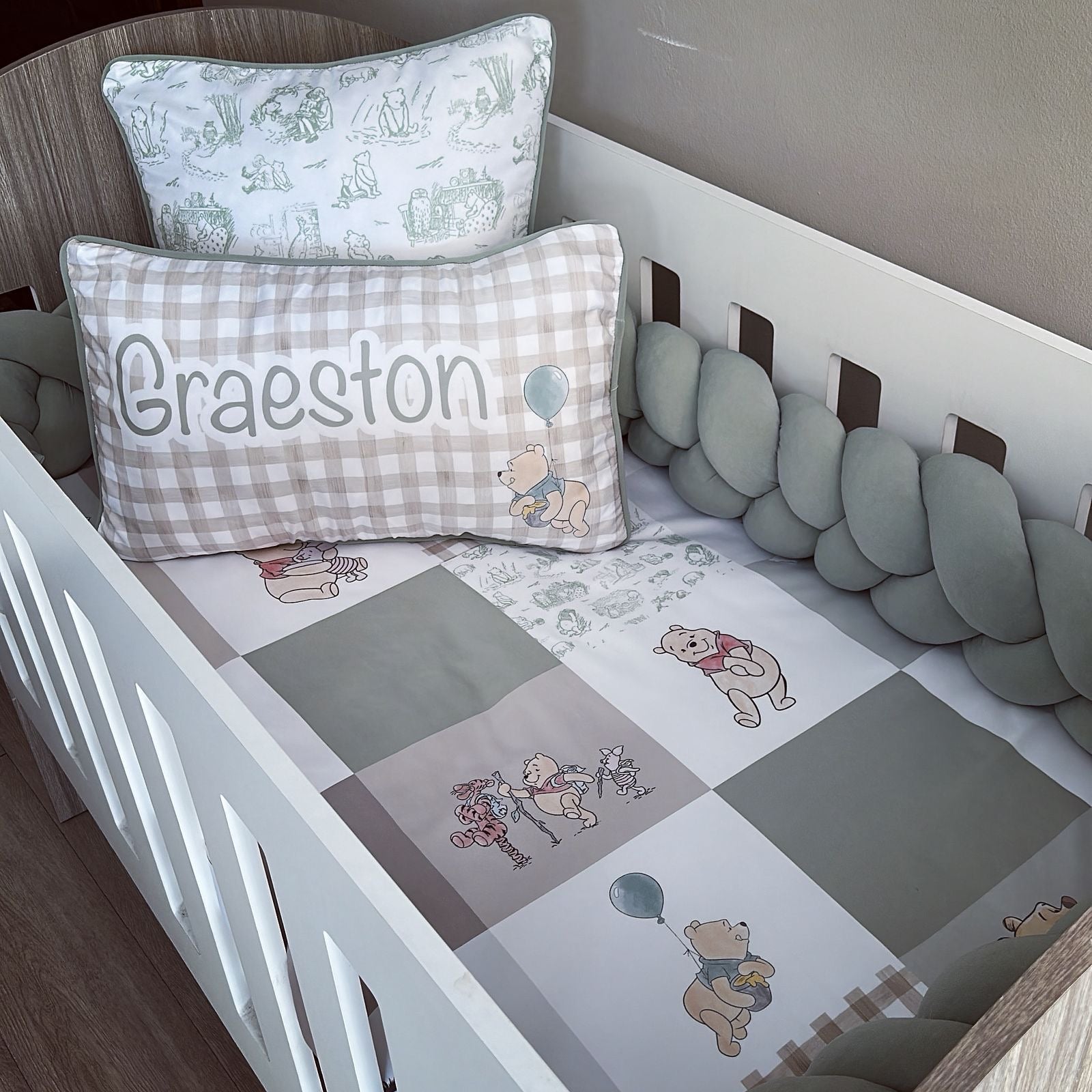 Baby crib with checkered sheet, teddy bear design, and personalized pillow.