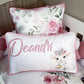 Decorative pillow with floral design and 'Deandri' branding on a bed.