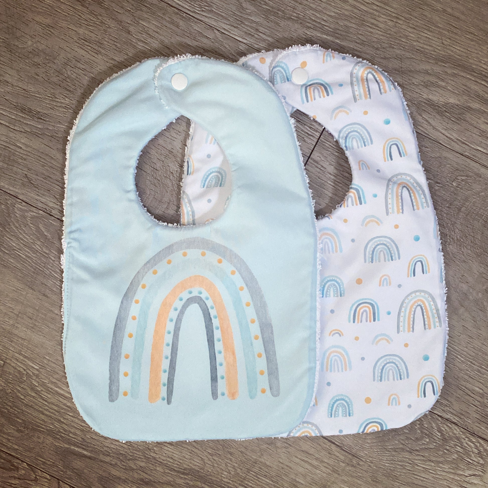 Two baby bibs with rainbow patterns on a wooden surface