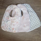 Three baby bibs with floral, checkered, and plain designs on a wooden surface. | Baby Essentials | All Baby Products | Soft Spot Kids | South Africa