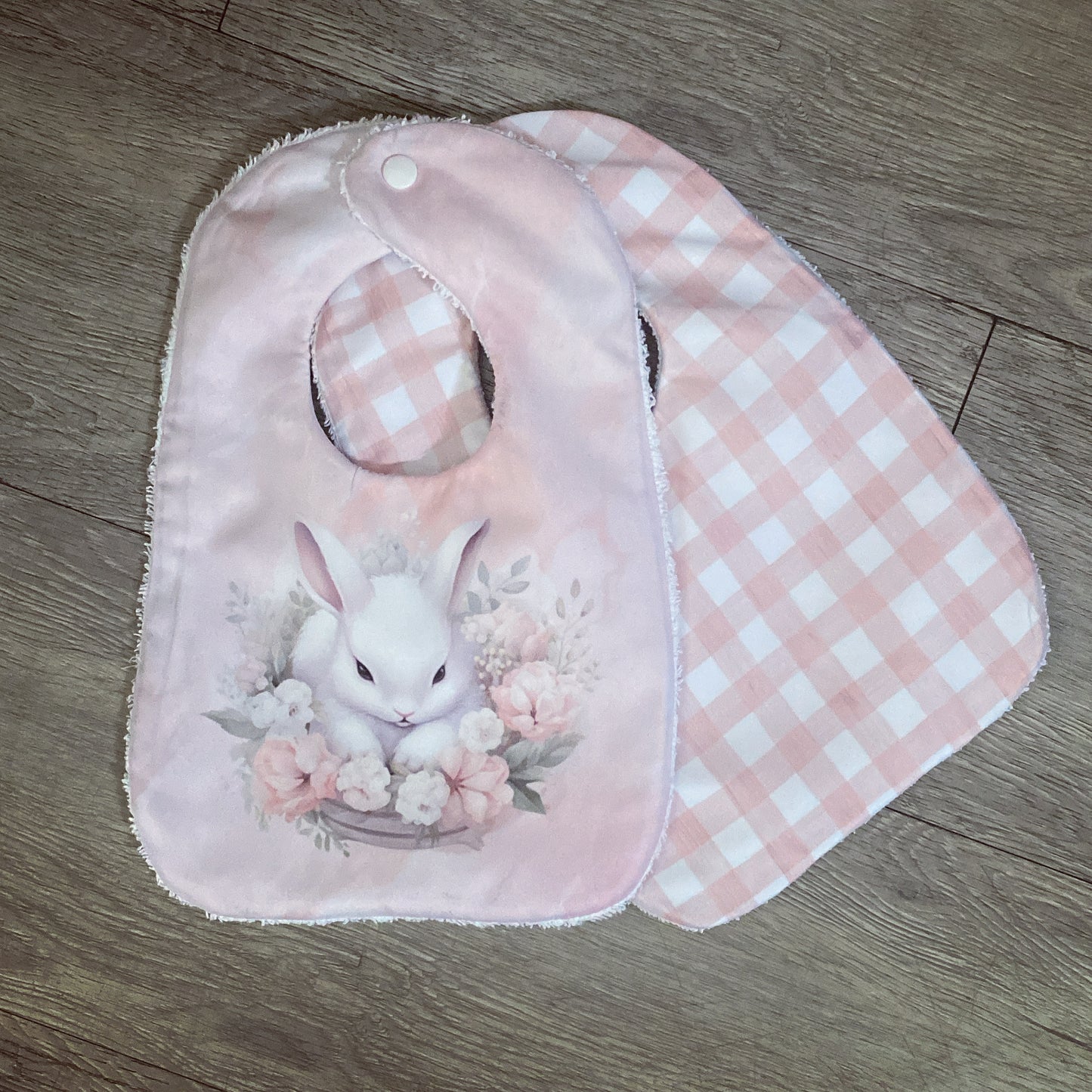 Pink baby bib and burp cloth with a bunny design on a wooden surface