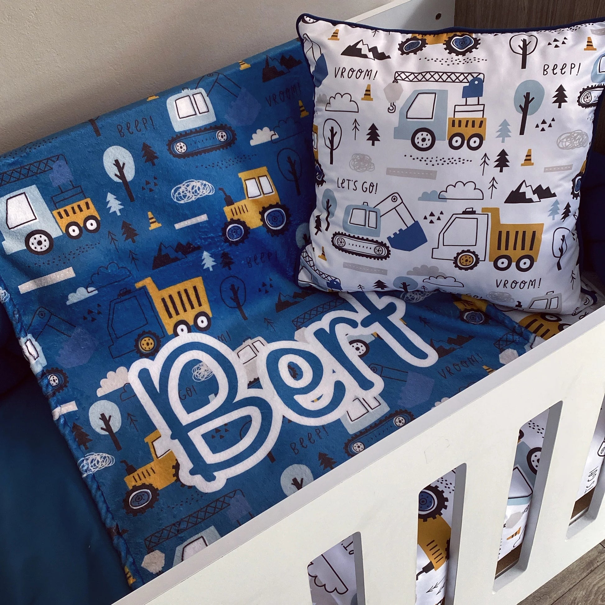 Children's bedding set with truck patterns and a pillow featuring construction vehicles on a crib.