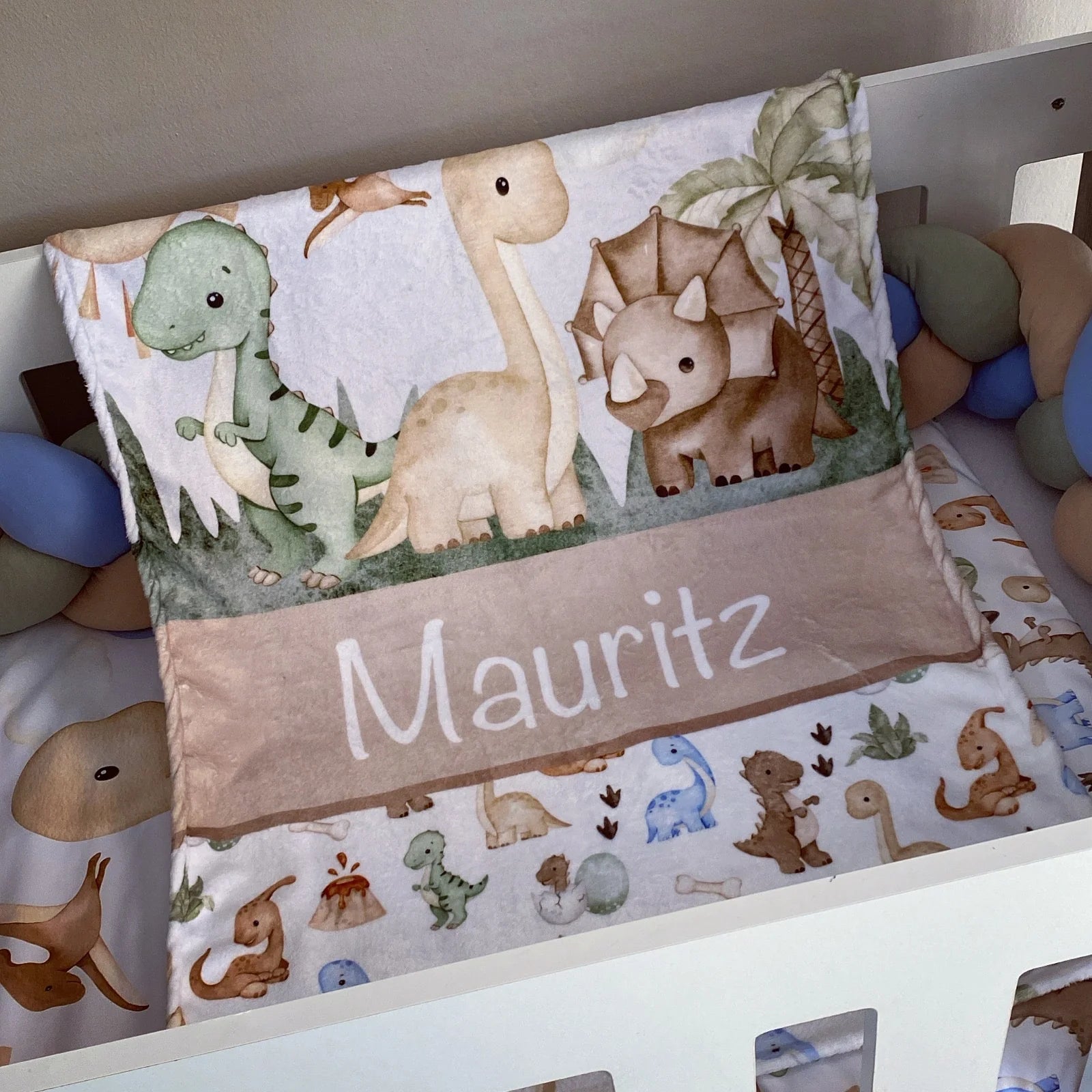 Crib bumper with dinosaur pattern and personalized name 'Mauritz' on a crib.