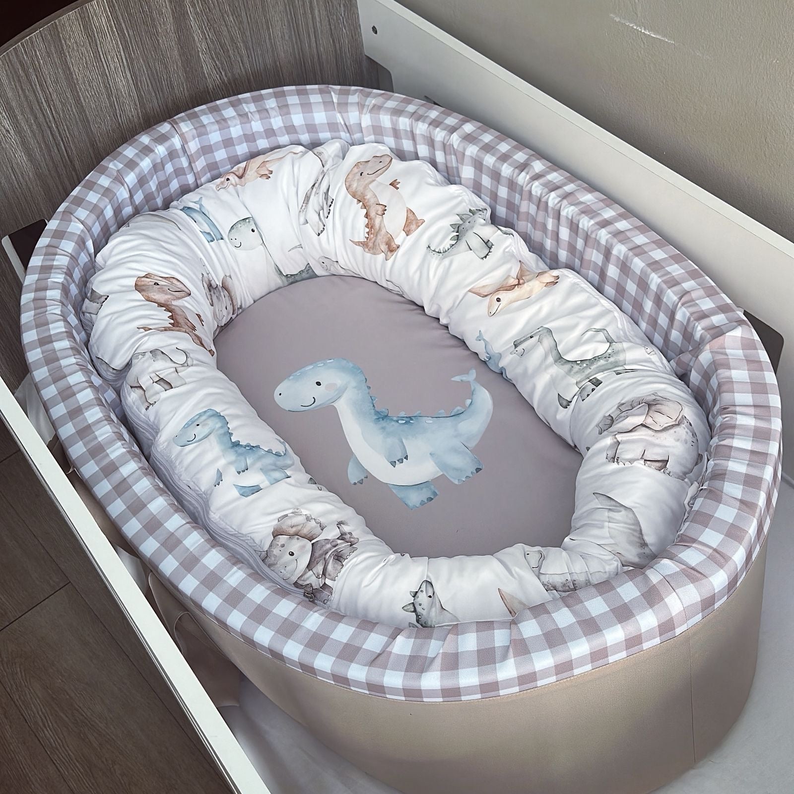 Baby crib with dinosaur-themed bedding in a checkered crib bumper.