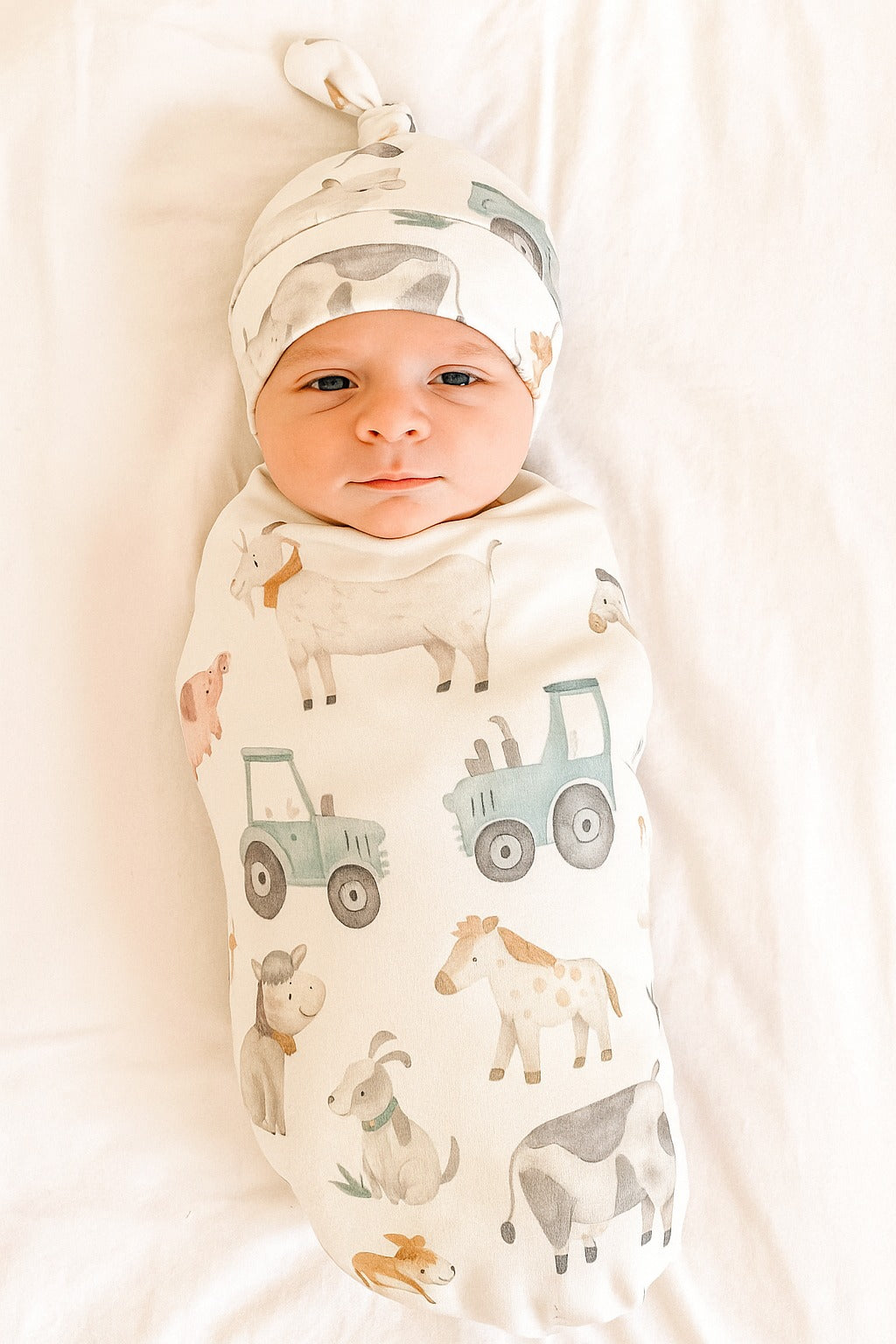 Newborn baby wrapped in a swaddle with farm animal prints and wearing a matching hat.