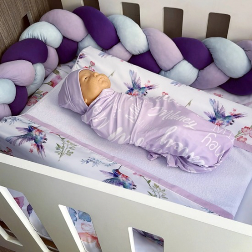 Baby swaddled in a floral blanket with 'Honey my love' text in a crib with colorful bumper pads.