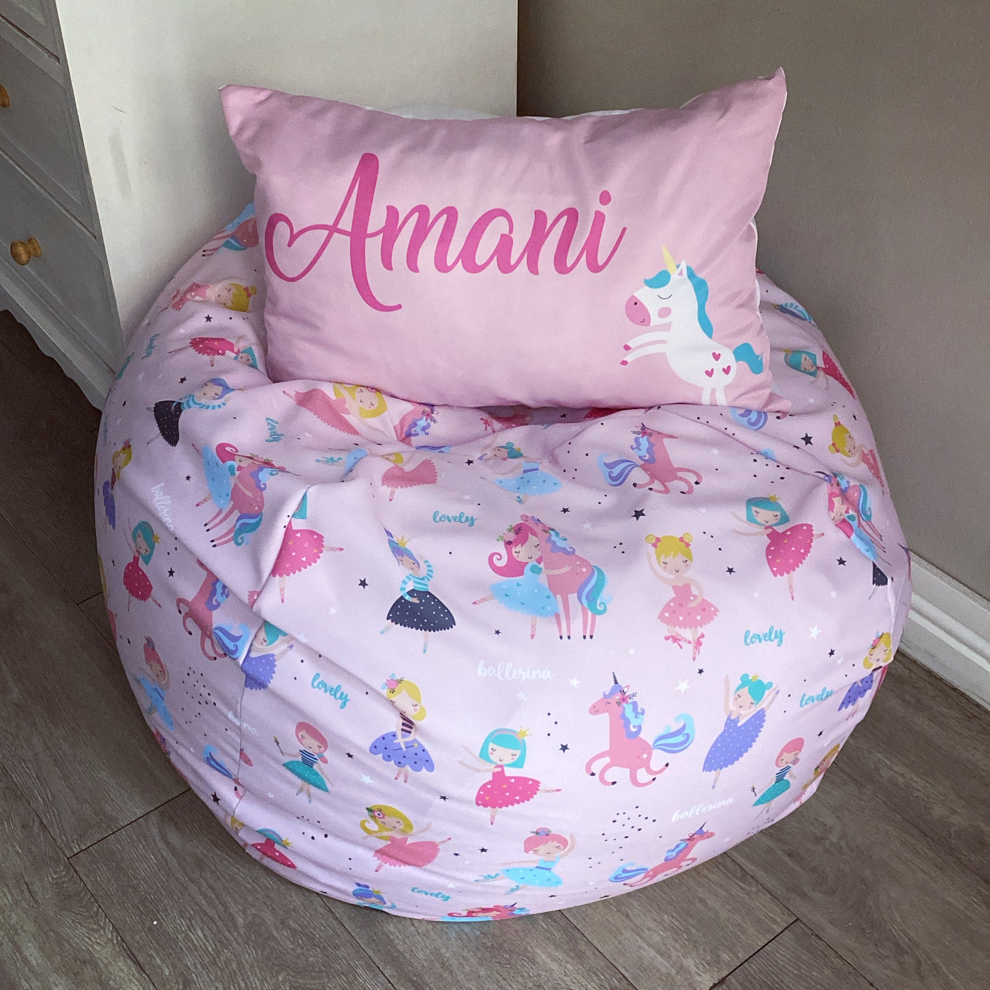 Children's bean bag chair with unicorn and fairy pattern and matching pillow with 'Amani' on a wooden floor.