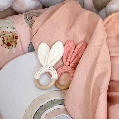 Two baby teething rings, one white and one pink, on a soft fabric background.
