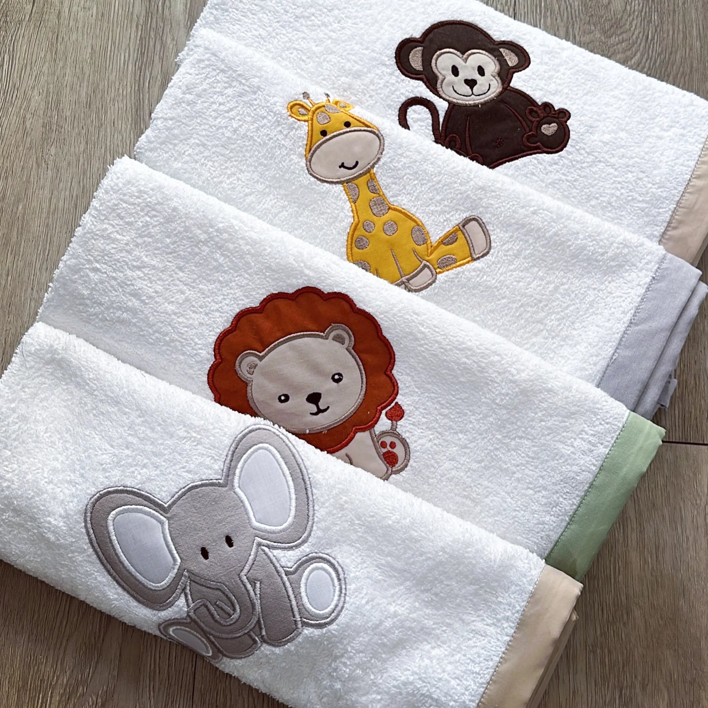 Two white towels with embroidered animal designs on a wooden surface