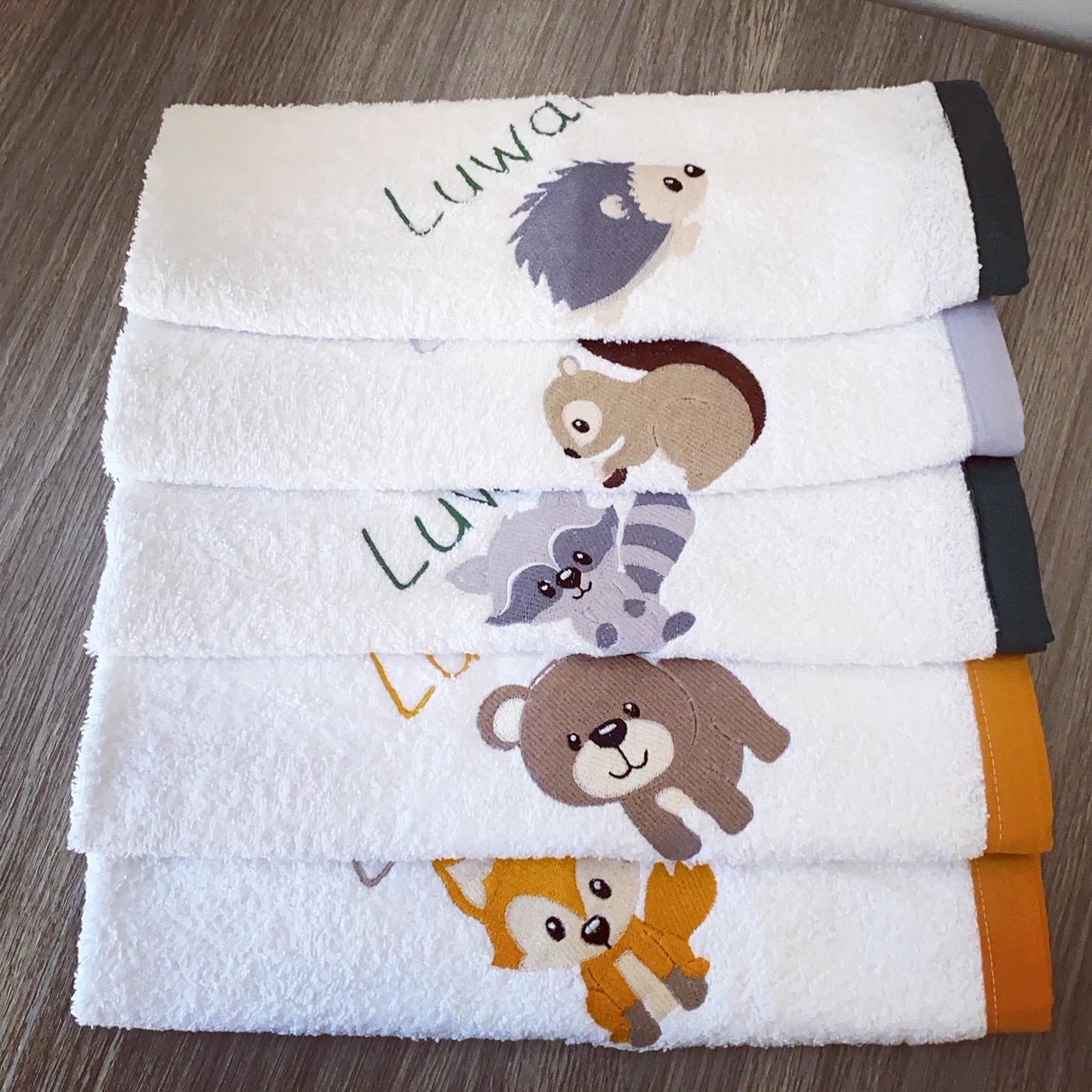 Stack of towels with animal designs and 'Luwa' branding on a wooden surface