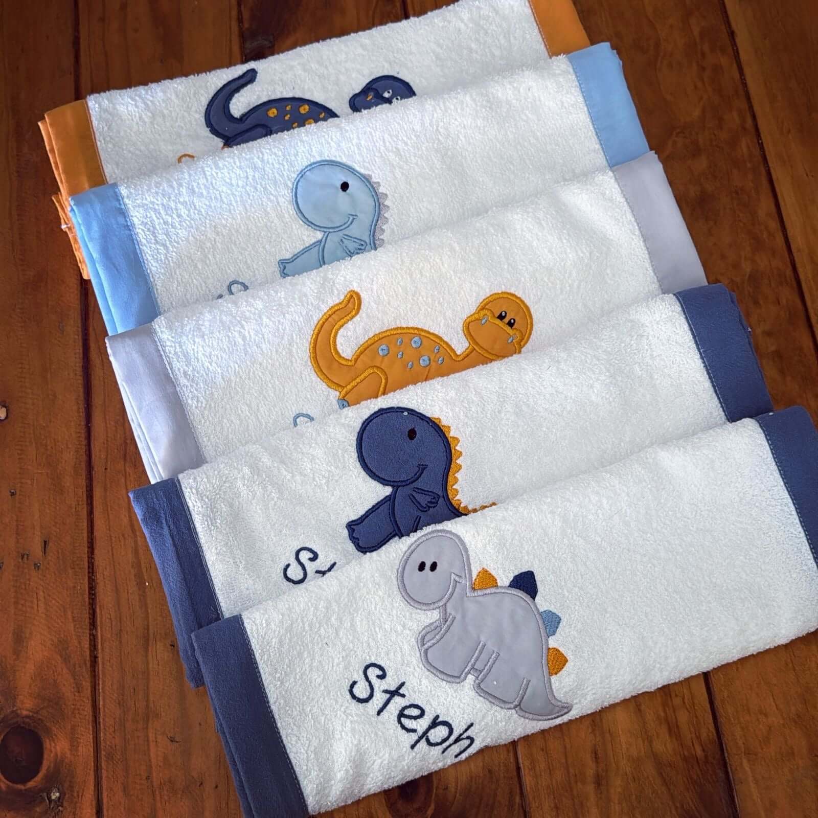 Set of four baby burp cloths with dinosaur designs on a wooden surface