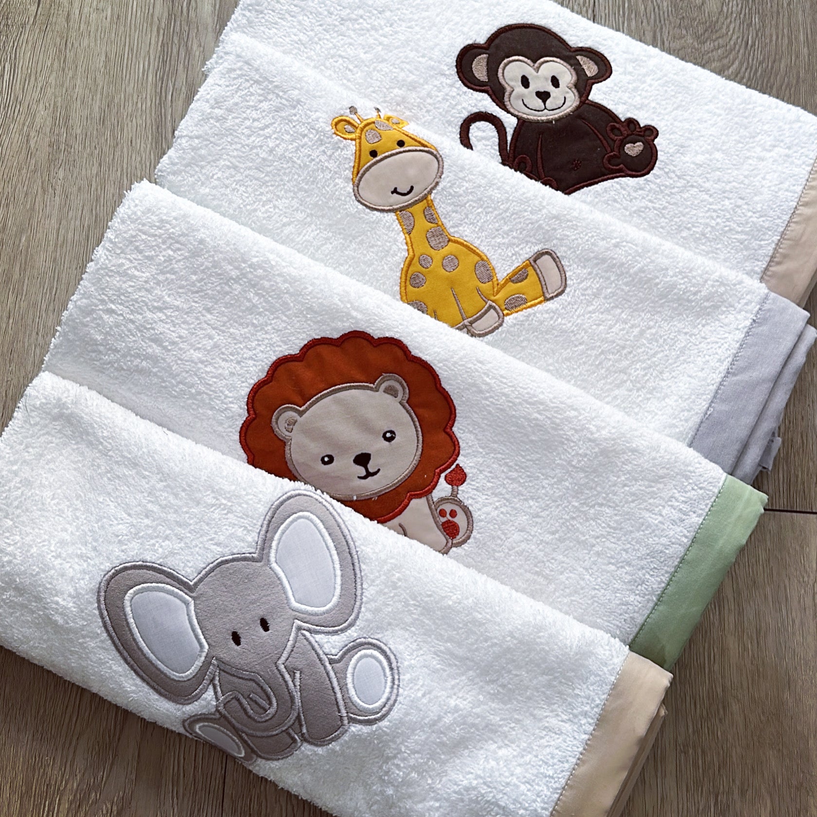 A set of white burp cloths with embroidered animals including a monkey, giraffe, elephant, and lion.