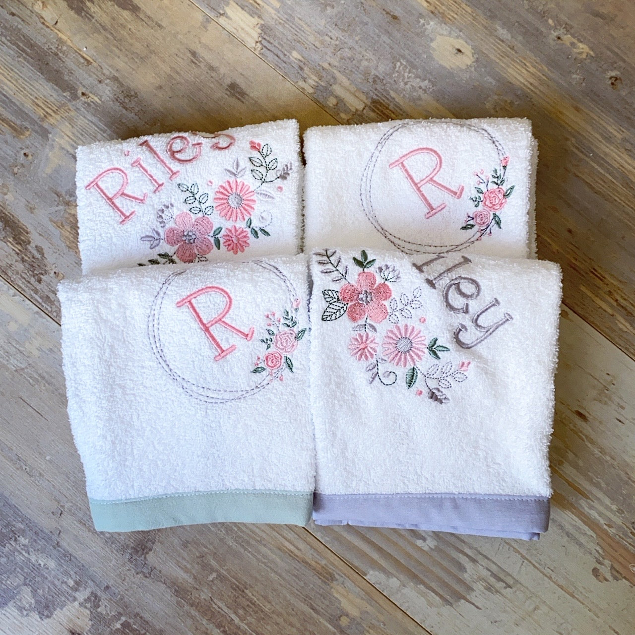 Four white towels with floral embroidery and monograms on a wooden surface