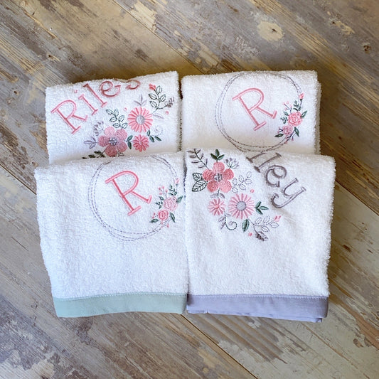 Four white towels with floral embroidery and monograms on a wooden surface