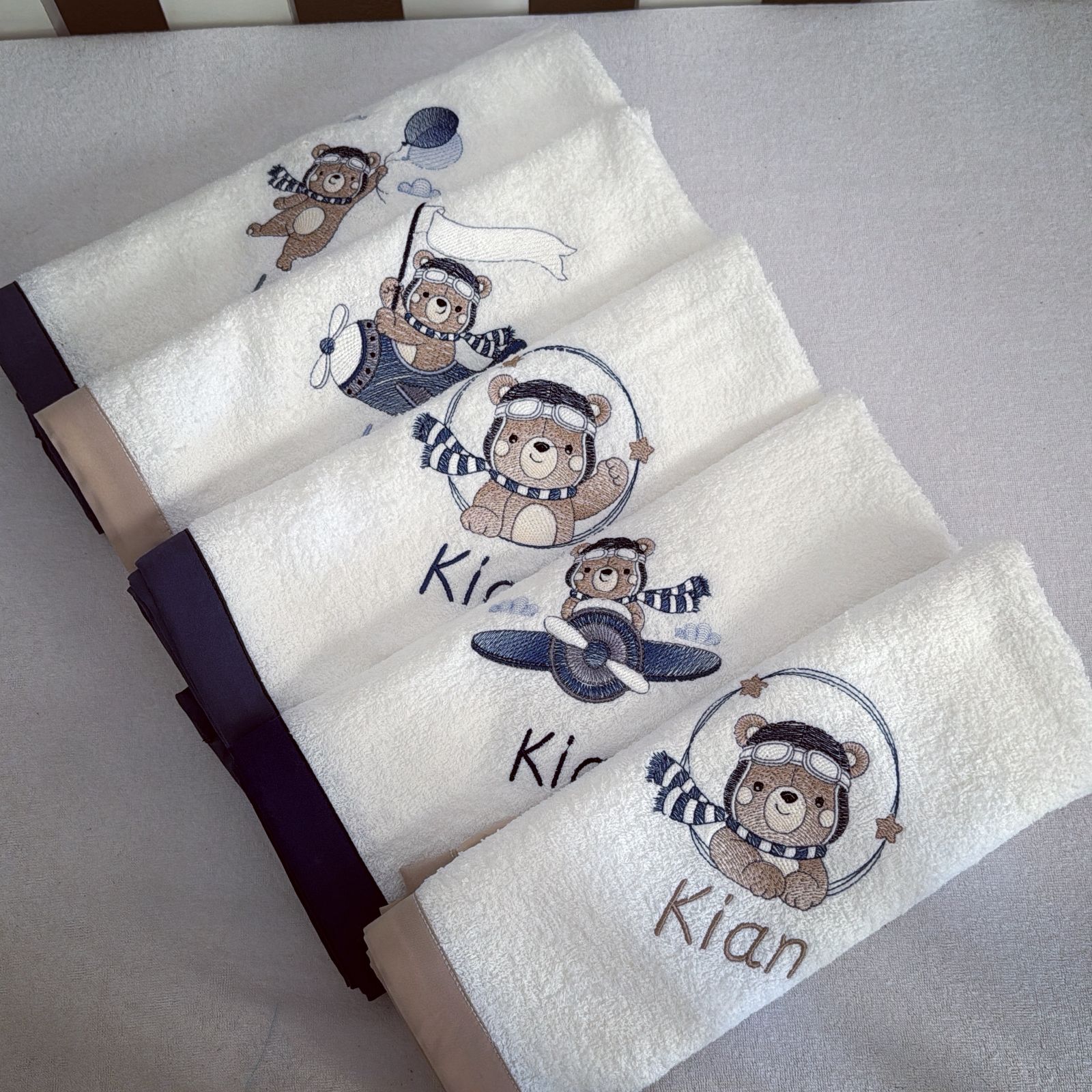 Set of towels with embroidered teddy bear designs and the name 'Kian' on a light gray background.