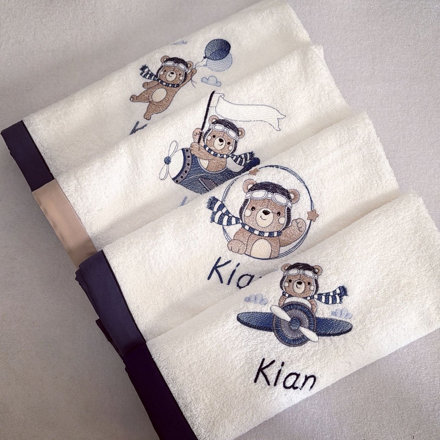 Folded towel with embroidered teddy bears and names on a light gray background