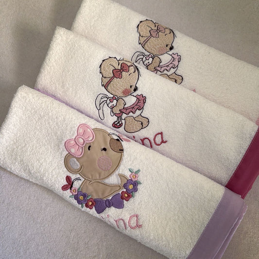 White towels with embroidered teddy bear designs and names on a neutral background