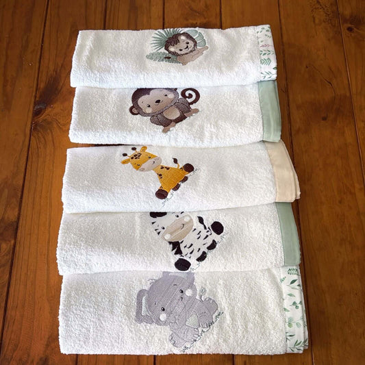 Set of five white towels with embroidered animal designs on a wooden floor.