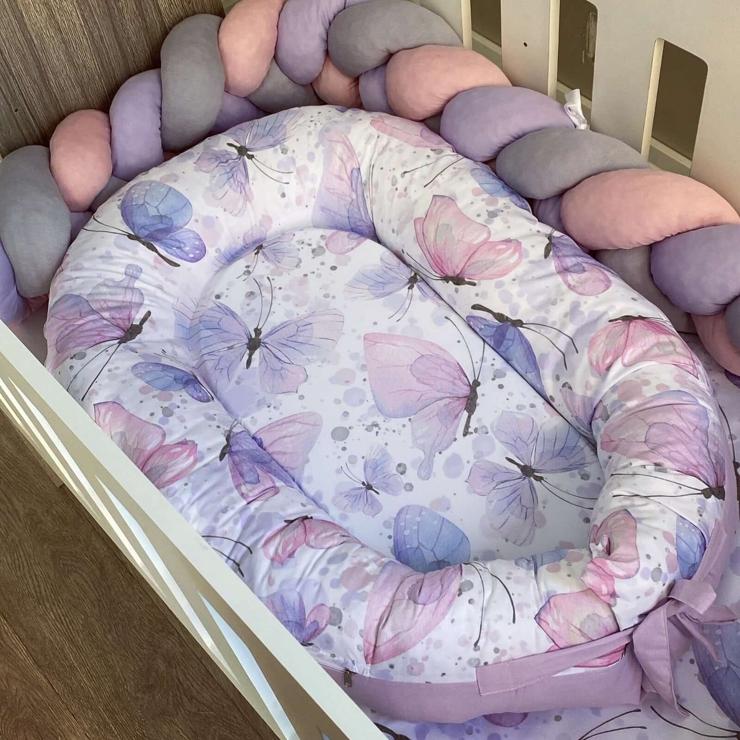 Baby nest with butterfly pattern surrounded by colorful round pillows.