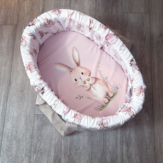 Baby carry cot with pink interior and rabbit design on a wooden floor