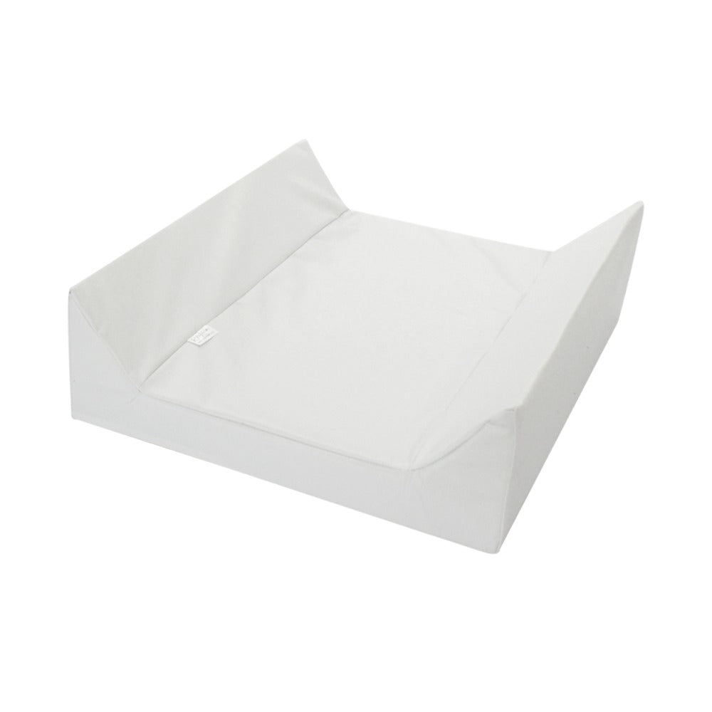 A white fabric changing pad or cushion with a raised rectangular base and angled top, shown on a plain white background.