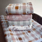 Stack of folded fabric sheets with patterns on a wooden surface. | All Nursery Sets | Baby Bedding Sets South Africa | Soft Spot Kids | South Africa