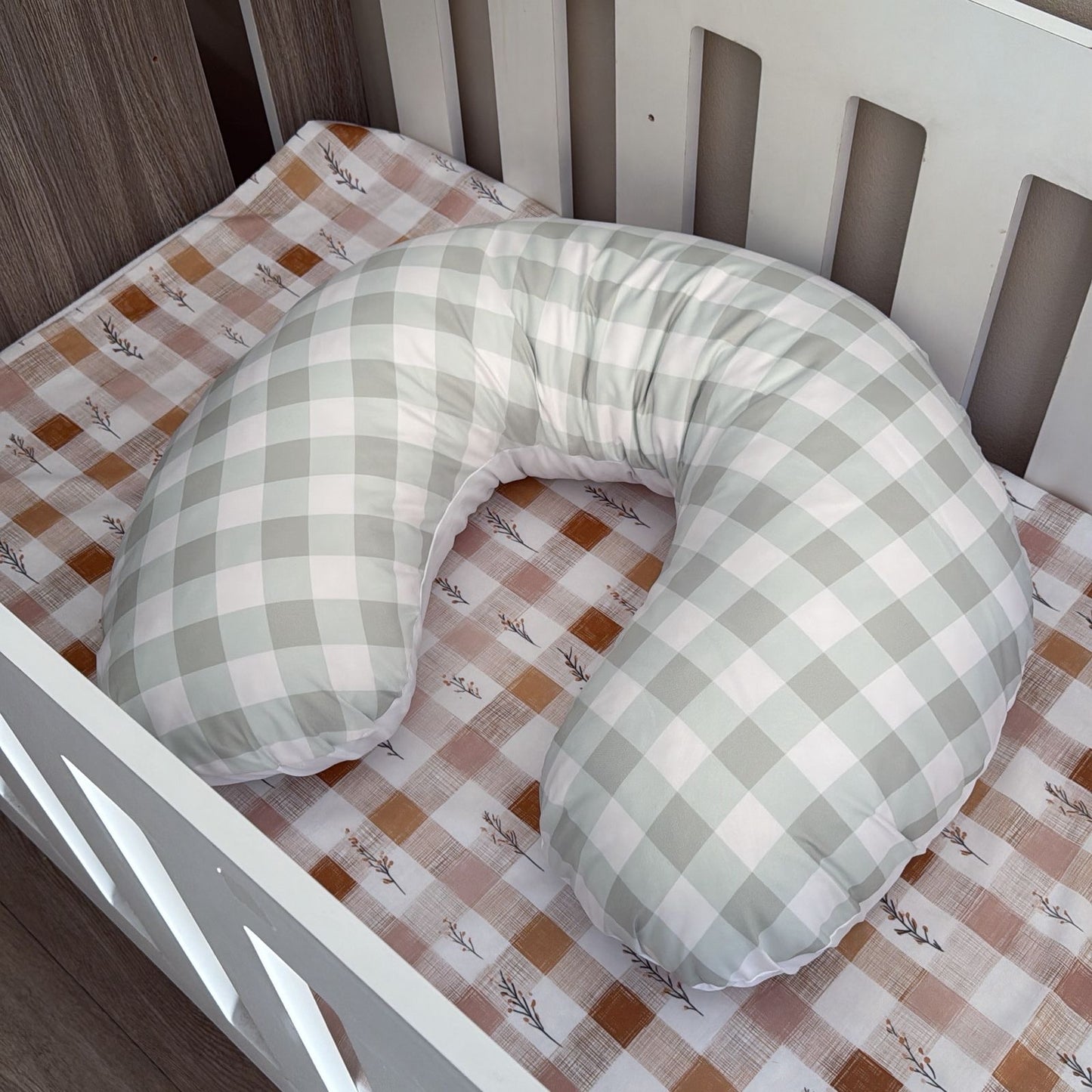 Green and white checkered U-shaped pillow on a crib with a patterned sheet.