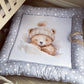 A padded baby floor mat or play mat with a gray star-patterned border and a white center, featuring a watercolor illustration of a teddy bear wearing a cream knit hat. The mat is placed on a wooden floor next to a crib. | All Nursery Sets | Baby Bedding Sets South Africa | Soft Spot Kids | South Africa