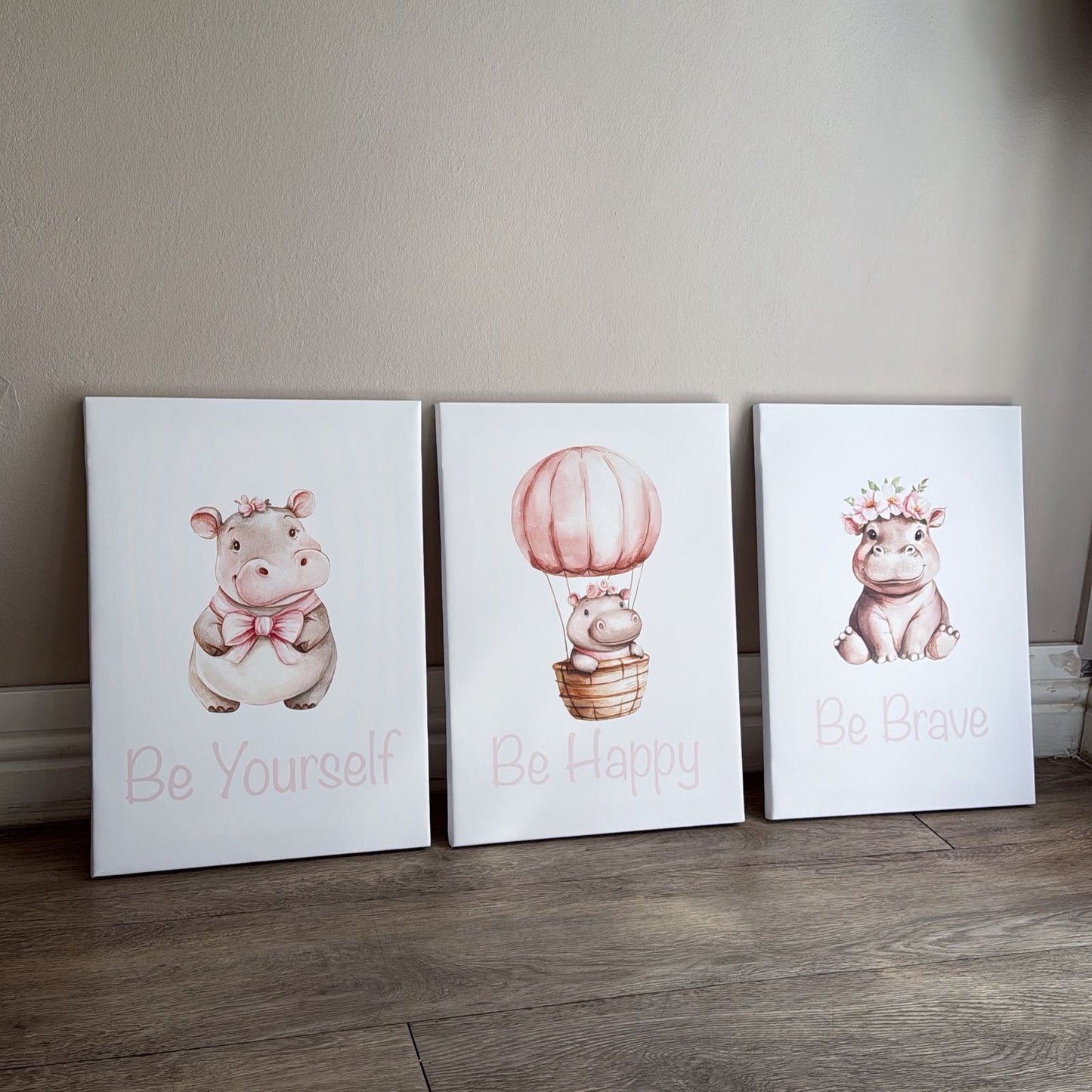 Three wall art prints featuring cartoon hippopotamuses with motivational phrases on a wooden floor.