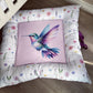 A square decorative cushion with a colorful hummingbird illustration on a light pink center panel, surrounded by a white floral border, photographed on a wooden floor. | All Nursery Sets | Baby Bedding Sets South Africa | Soft Spot Kids | South Africa