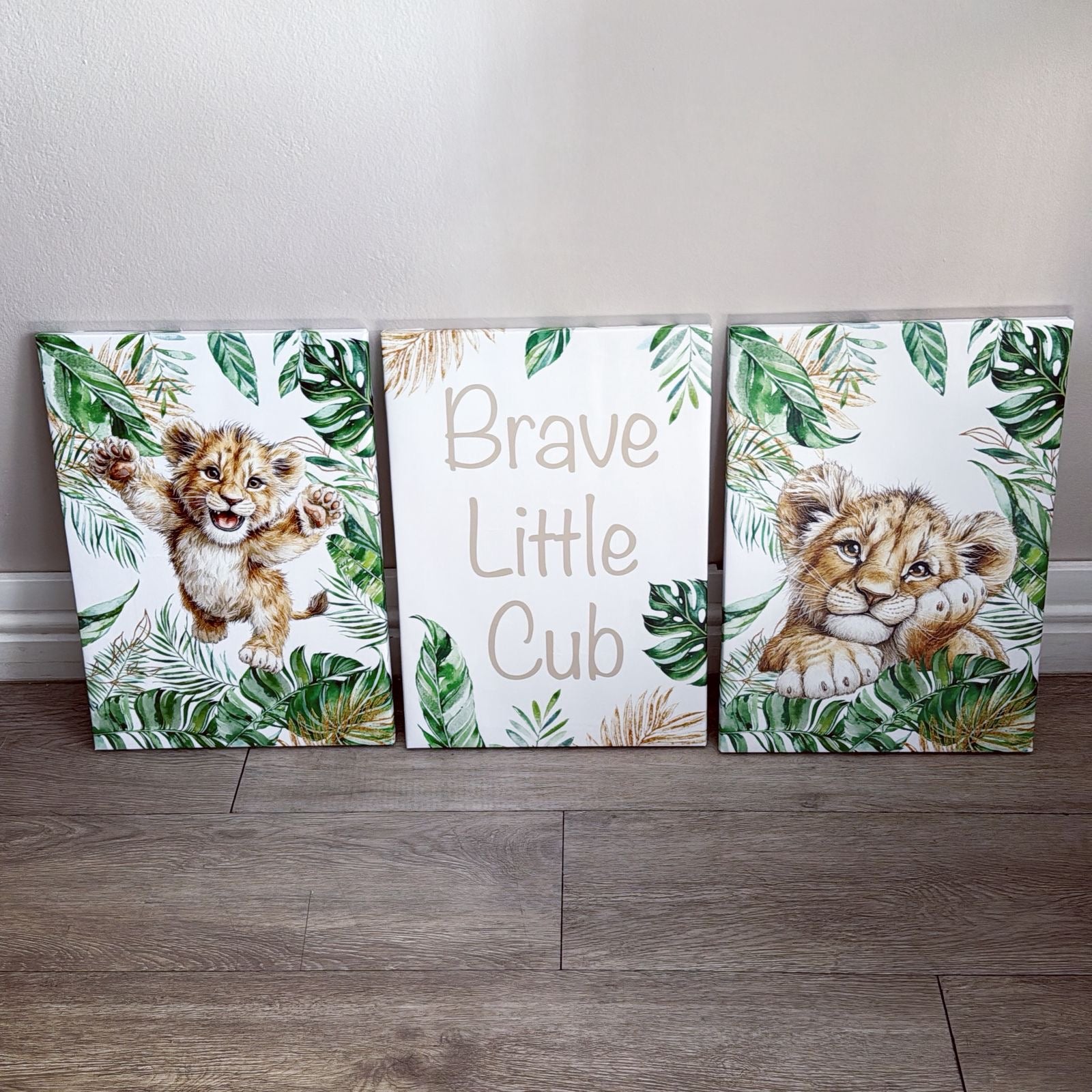 Three canvas prints with lion cub illustrations and text on a wooden floor.