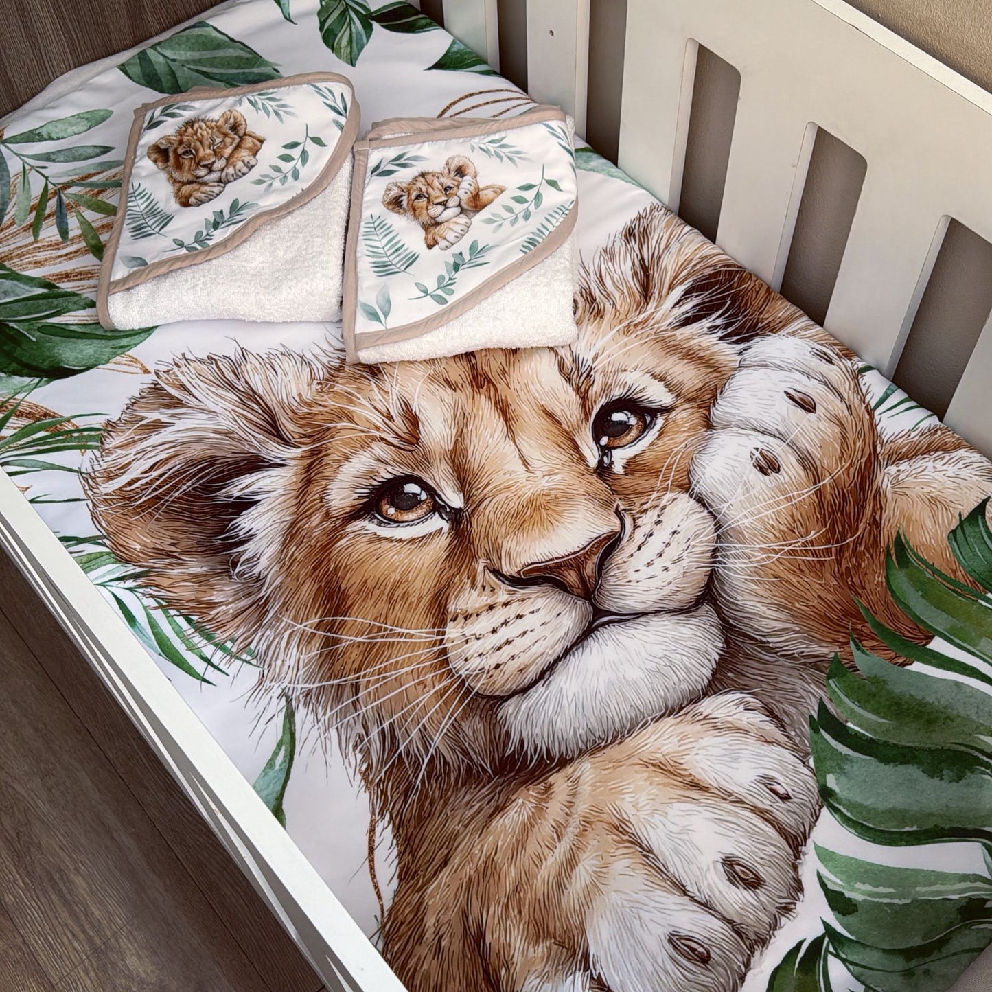 Crib with lion-themed bedding and towels on a wooden floor.