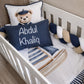 A personalized baby crib bedding set featuring a white crib with a watercolor sailboat print, a navy blue personalized pillow reading 'Abdul Khaliq', a white pillow with a teddy bear wearing a captain hat, and a chunky braided bumper in navy, white, and beige. | All Nursery Sets | Baby Bedding Sets South Africa | Soft Spot Kids | South Africa