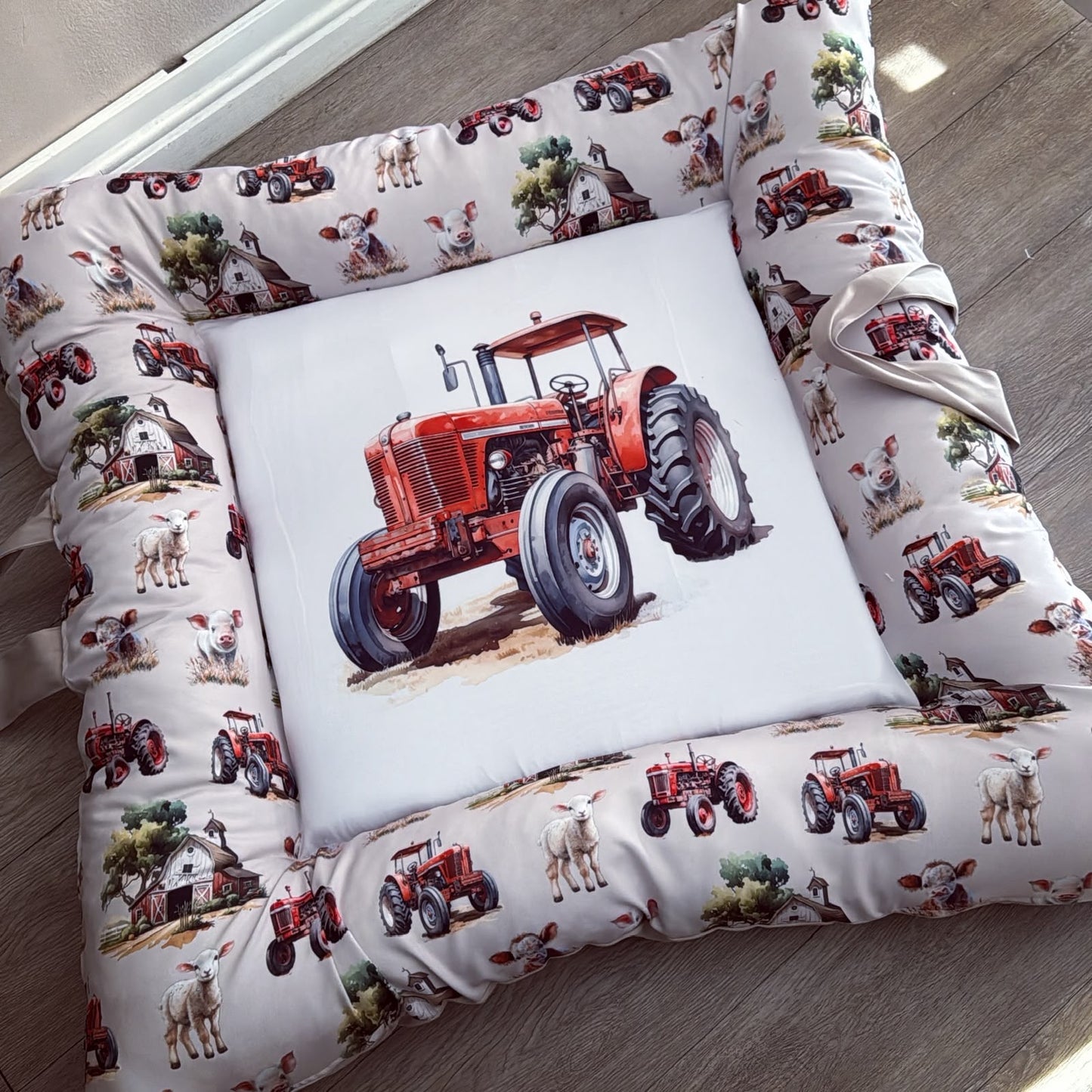 A square farm-themed pet bed with a white background and a printed border of red tractors, cows, sheep, barns, and trees, featuring a large central white square patch with a red tractor illustration.
